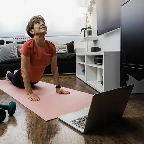 Woman stretching in a cobra pose on a yoga mat at home, following an online session on her laptop